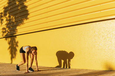 Weibliche Athletin beugt sich beim Training vor einer gelben Wand - MGRF00455
