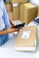 Young woman scanning bar code of package at studio - GIOF13446