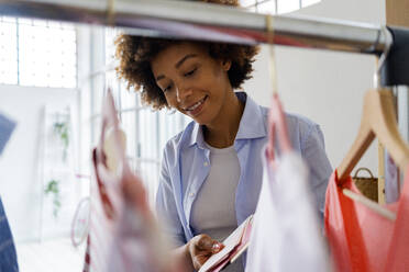 Female fashion designer arranging clothes in rack at studio - GIOF13467