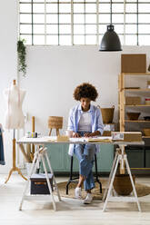 Businesswoman sitting at desk while working at studio - GIOF13472