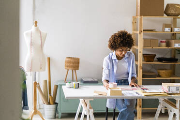 Weibliche Designerin sitzt am Schreibtisch und arbeitet im Studio - GIOF13474