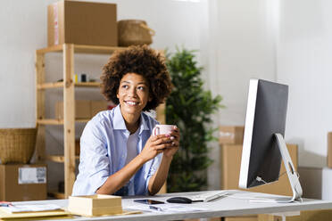 Thoughtful Afro businesswoman holding mug at desk in studio - GIOF13480