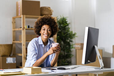 Happy young businesswoman holding mug at desk in studio - GIOF13481