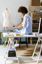 Geschäftsfrau, die ein digitales Tablet benutzt, während sie in einem Studio am Schreibtisch sitzt - GIOF13493