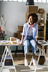 Businesswoman looking away while sitting on desk at studio - GIOF13500