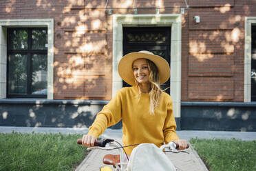 Happy woman standing with bicycle in front of building - VPIF04823