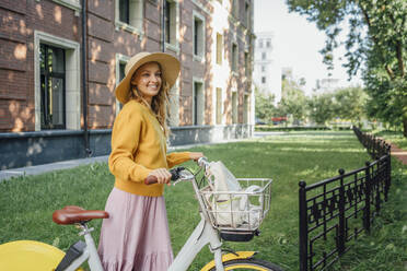 Young woman looking away while standing with bicycle near building - VPIF04824