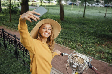 Lächelnde Frau nimmt Selfie mit Fahrrad durch Smartphone im Park - VPIF04826