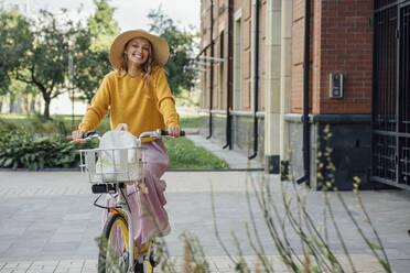 Glückliche junge Frau fährt Fahrrad in der Nähe eines Gebäudes - VPIF04827