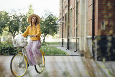 Frau mit Hut fährt mit dem Fahrrad an einem Gebäude vorbei - VPIF04828