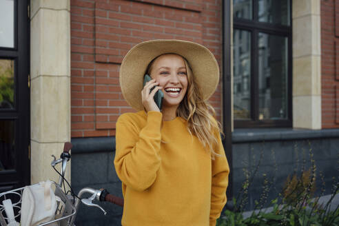 Fröhliche junge Frau, die vor einem Gebäude mit einem Mobiltelefon spricht - VPIF04843