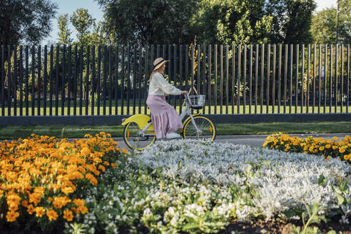 Junge Frau fährt Fahrrad am Zaun eines Parks - VPIF04849