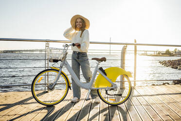 Junge Frau mit Fahrrad an der Strandpromenade an einem sonnigen Tag - VPIF04869