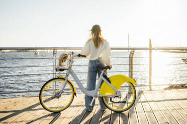 Frau mit Fahrrad schaut auf das Meer, während sie an der Strandpromenade steht - VPIF04870