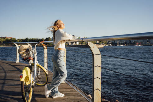 Frau mit Fahrrad am Geländer der Strandpromenade stehend - VPIF04874