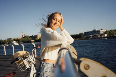 Beautiful smiling young woman with head in hand leaning on railing - VPIF04875