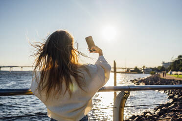 Junge Frau nimmt Selfie durch Smartphone durch Geländer - VPIF04879