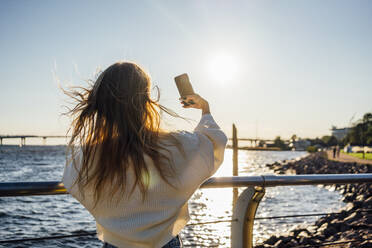 Young woman taking selfie through smart phone by railing - VPIF04879