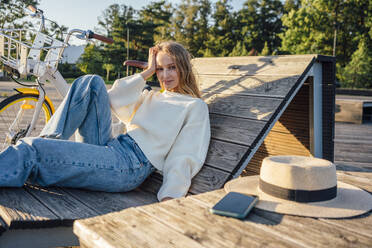 Blond woman with head in hand relaxing on wooden bench - VPIF04885