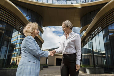 Geschäftsfrauen schütteln sich die Hände, während sie vor einem Gebäude stehen - LLUF00060