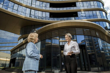 Smiling businesswomen having discussion standing in front of building - LLUF00062