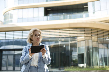 Nachdenkliche Geschäftsfrau, die ein digitales Tablet hält, während sie vor einem Bürogebäude steht - LLUF00065