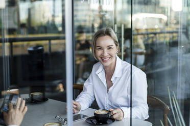 Smiling businesswoman having coffee with coworker at cafe - LLUF00074