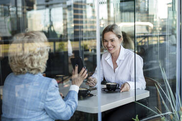 Businesswomen discussing while sitting in cafe seen through glass window - LLUF00075