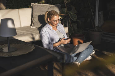 Eine Freiberuflerin benutzt ihr Handy bei der Arbeit auf der Terrasse - UUF24707