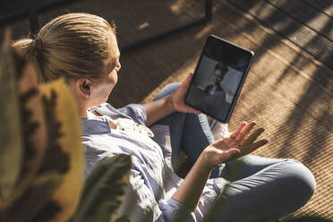 Frau im Gespräch mit einem Freund per Videoanruf über ein digitales Tablet auf einer Terrasse - UUF24708
