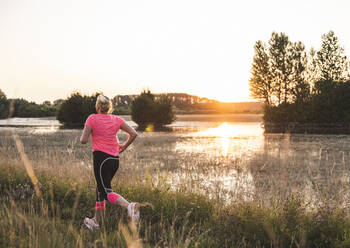 Woman exercising while running on grass during sunset - UUF24711