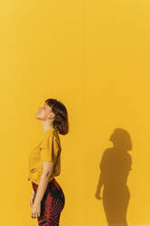 Woman standing with eyes closed by yellow wall - MGRF00459