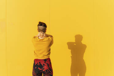 Woman with hands on neck standing in front of yellow wall - MGRF00462