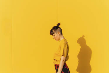 Androgynous person with half-shaved hairstyle standing by yellow wall - MGRF00463