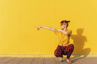 Androgynous person pointing while crouching on footpath - MGRF00466