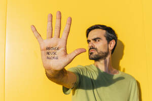 Junger Mann mit einer Nachricht auf der Handfläche vor einer gelben Wand stehend - MGRF00489
