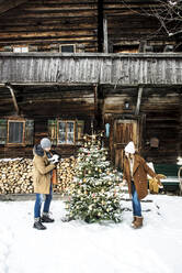 Ehepaar schmückt Weihnachtsbaum im Schnee stehend - HHF05662