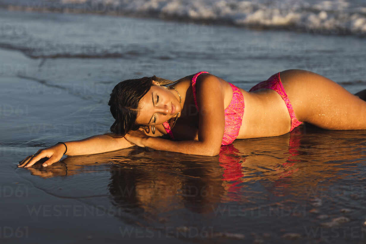 Young woman in bikini lying in shallow … – License image