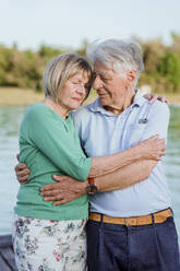 Älteres Paar mit geschlossenen Augen umarmt sich am See - AANF00013