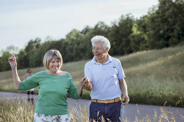 Fröhliches älteres Paar, das sich beim gemeinsamen Spaziergang an den Händen hält - AANF00015