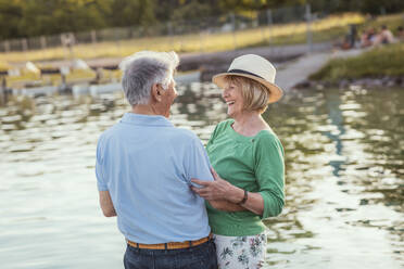 Cheerful senior couple looking at each other while standing by lake - AANF00029