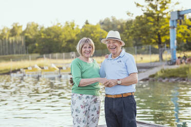 Fröhliches Paar, das am See stehend die Hände hält - AANF00033