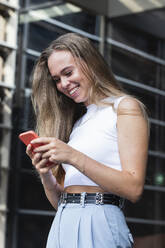 Happy blond businesswoman text messaging through mobile phone - PNAF02319