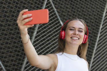 Glückliche Freiberuflerin mit drahtlosen Kopfhörern, die ein Selfie über ihr Smartphone macht - PNAF02326