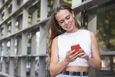 Blonde Geschäftsfrau lächelt bei der Benutzung eines Mobiltelefons - PNAF02327