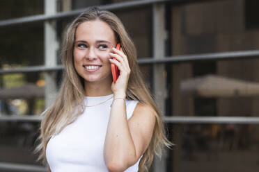 Lächelnde Geschäftsfrau mit langen blonden Haaren, die mit einem Smartphone telefoniert - PNAF02328