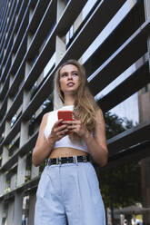 Female freelancer with mobile phone standing in front of building - PNAF02338