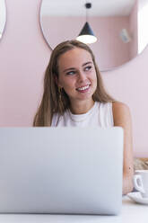 Smiling blond businesswoman with laptop sitting in cafe - PNAF02342