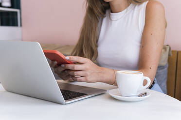 Geschäftsfrau mit Laptop und Mobiltelefon in einem Café - PNAF02345