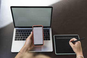 Female graphic designer using mobile phone and graphic tablet on cafe table - PNAF02355